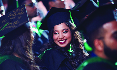 Smiling student of color in cap and gown at graduation.