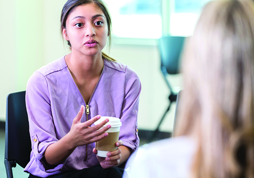 Young woman with serious expression talking to another woman facing her.